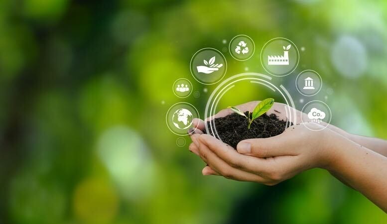 A pair of hands gently cups a small green seedling growing in soil, with circular eco-friendly icons symbolizing sustainability—like leaves, a globe, and recycling—digitally overlaid above the plant, set against a blurred green natural background.